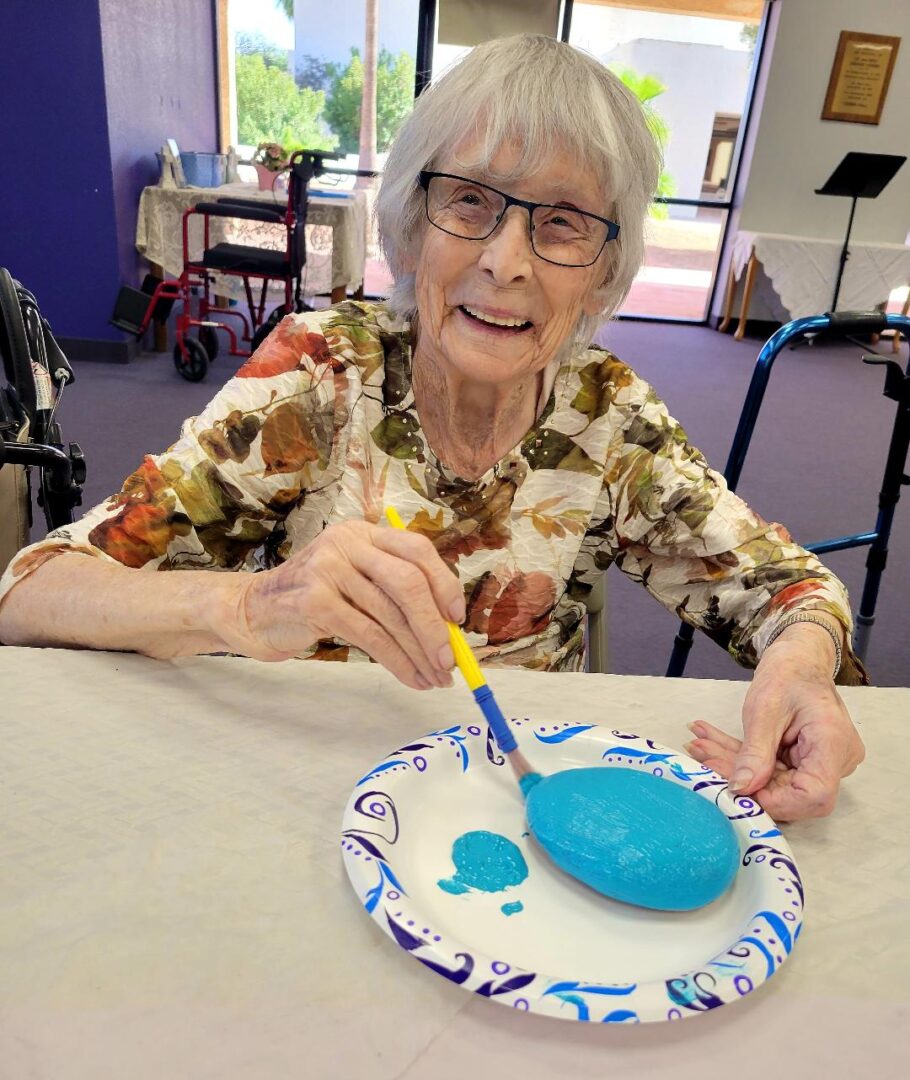 old woman smiling and painting a rock